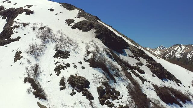 Aerial drone dolly shot ascending up the side of a mountain side in melt in spring at the Cerro Bayo ski resort near Villa La Angostura, revealing forest and rocks on the mountains