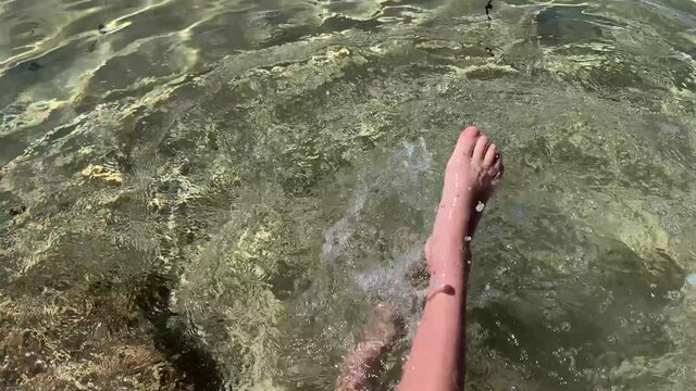 Inspiring closeup of active boy s legs doing bycicle movements while sitting on the beach and making thousands of water splurges