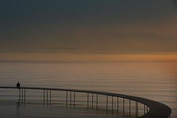 Person sitting alone on abridge looking at the sea before sunrise.