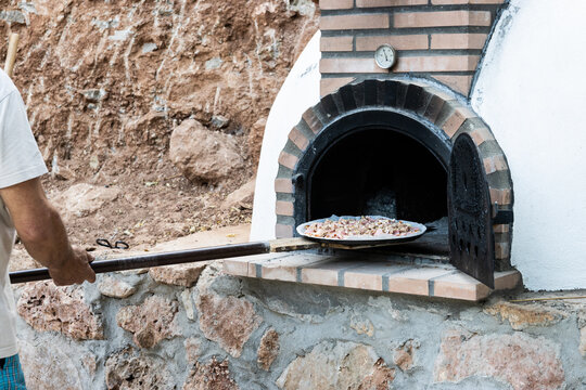 Man putting pizza in handmade white painted wood oven built outdoors with shovel