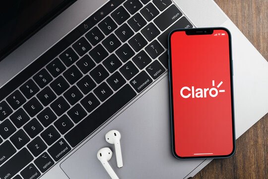 Claro, telecommunications company, app on the smartphone screen on wooden background with a computer beside it. Office environment. Rio de Janeiro, RJ, Brazil. October 2021.