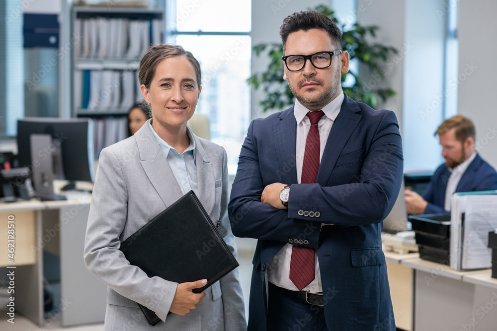 Poster two well-dressed employees standing in front of camera in office environment
