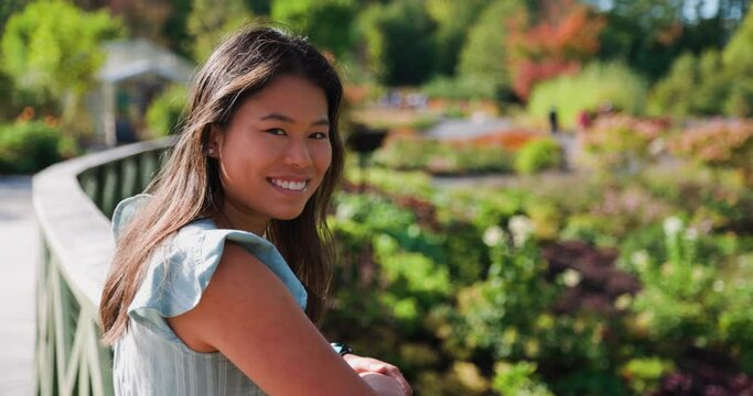 Beautiful Asian woman looking towards camera and smiling in beautiful vibrant park