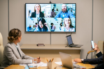 Several business people on large display hanging on wall of boardroom where group of employees having webinar