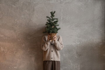 Young pretty woman hold in hands pot with Christmas fir branches. Minimal fashion festive Christmas and New Year celebration concept.