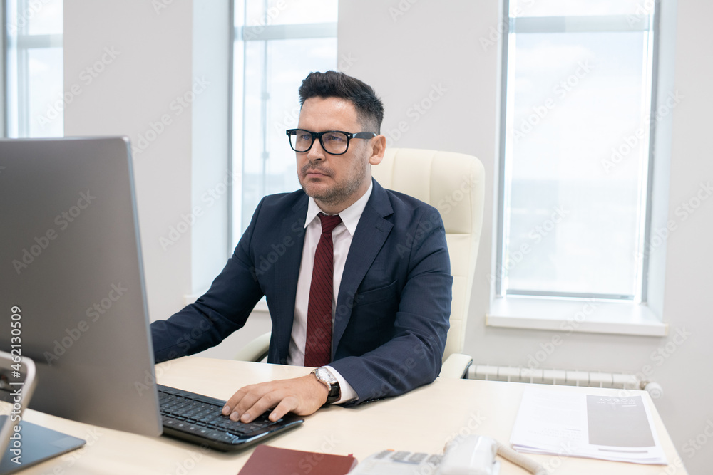 Poster director of contemporary company working over new business project in front of computer monitor