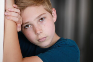 Portrait of casual young boy with face posing against arm, looking at the camera. One person. Family, model, childhood concept.