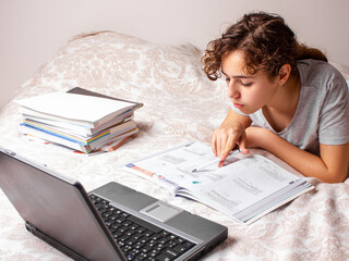 Teenager girl studying online at home. School girl with lap top on the bed. Home education