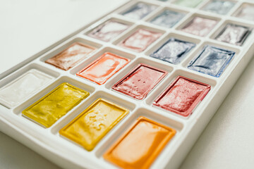 Bright watercolor paints on a white background. A place for text. The brush lies next to the paints. Multi-colored paints close-up
