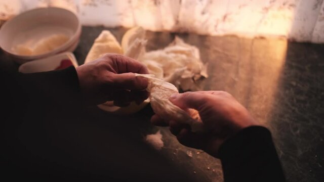 A man cleans a piece of pomelo with his hands in the kitchen