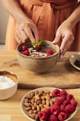 Hands of young woman putting mint leaf on top of appetizing dessert in bowl