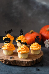 Festive Halloween cupcakes decorated with black toppings. Dark background with pumpkin and copy space, selective focus. Bakery menu