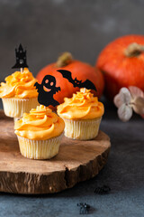Festive Halloween cupcakes decorated with black toppings. Dark background with pumpkin, selective focus. Bakery menu. Close up