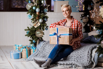 Obraz na płótnie Canvas Beautiful girl in a red plaid shirt sits with Christmas gifts on Christmas and New Year's Eve. Merry Christmas and Happy New Year. Happy and joyful emotions.