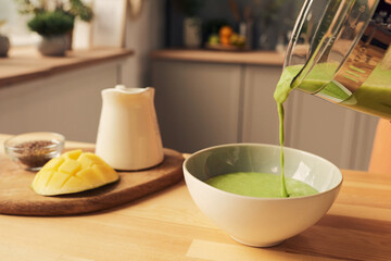 Someone holding blender while pouring fresh homemade vegetable smoothie into bowl