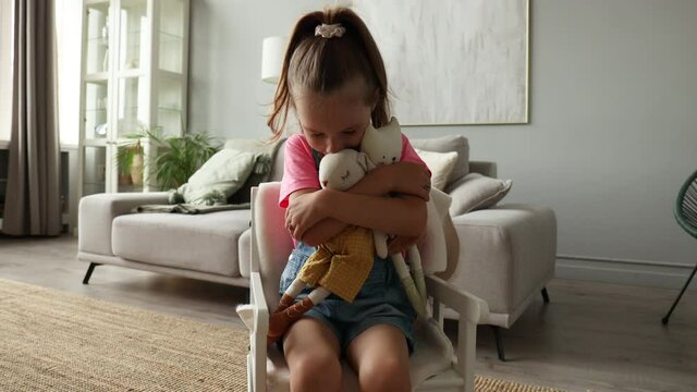 Excited child in rocking chair playing with her stuffed toys while sitting in living room at home.