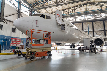 Big white passenger airplane on maintenance repair check in airport hangar indoors. Aircraft concept - obrazy, fototapety, plakaty