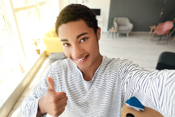 Happy African-American teenage boy taking selfie at home