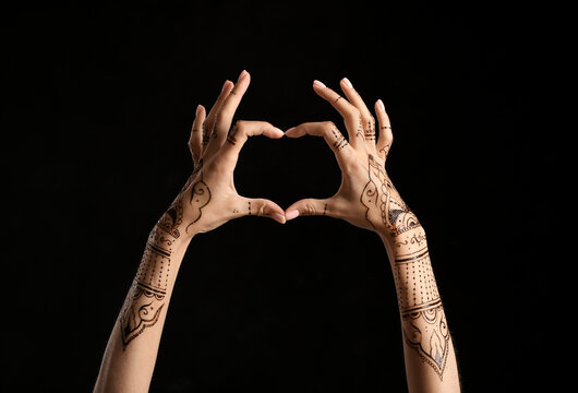 Female hands with henna tattoo making heart on dark background