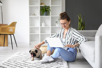 Young woman with cute pug dog using laptop at home