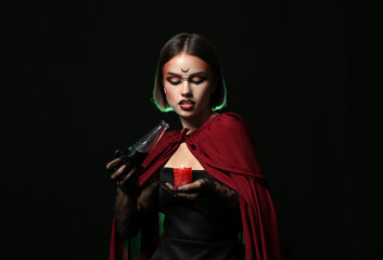 Naklejka premium Young witch with candle and potion on dark background