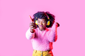 Young black woman listening music dancing holding smartphone wearing wireless headphones