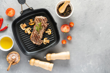 Grilled beef steak with mushrooms and spices on a grill pan on a gray background