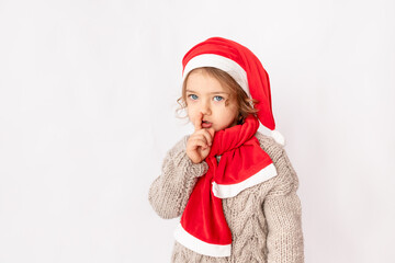 a little girl in a Santa hat shows her finger quietly on a white background, space for text