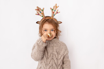 little girl with deer antlers and Christmas ball on her nose on white background, space for text, new year and Christmas concept