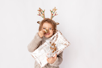 little girl with deer antlers and Christmas ball on her nose on a white background with a gift in her hands, space for text, new year and Christmas concept
