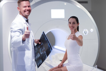 Smiling male doctor and female patient hold thumbs up in office for MRI examination