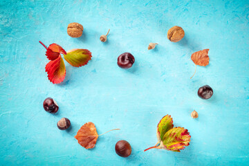 Autumn background with vibrant leaves and chestnuts in the shape of a heart, overhead flat lay shot on blue with a place for text, a design template for a banner or invitation