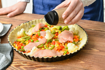 Woman preparing chicken pot pie with vegetables at kitchen table