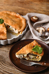 Baking dish and plate with piece of tasty chicken pot pie on wooden background