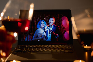 Birthday celebration. Online greeting. Distance meeting. Defocused cheering two glass of wine with happy couple congrats on laptop screen in dark room interior.