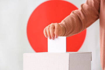 Obraz premium Japanese election voting process with hand placing ballot into box, democracy and citizen participation concept, the japanese flag serves as a background
