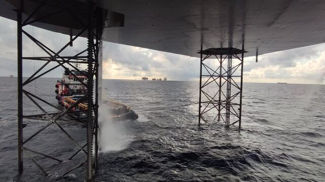 View Underneath Jack Up Drilling Rig In The Ocean with a supply boat and a central processing platform
