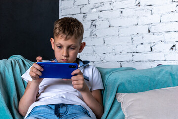 Boy sits on the sofa in the room and uses the phone to play.