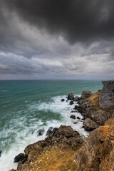 Fototapeta na wymiar Sea wave crashing on rocky coast with dark clouds