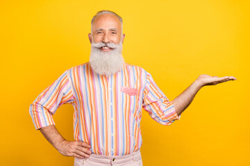 Portrait of attractive cheerful grey-haired man holding on palm copy blank space ad isolated over bright yellow color background