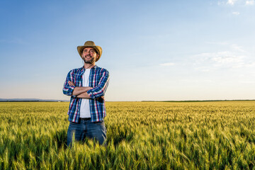 Farmer is standing in his growing wheat field. He is happy because of successful sowing.