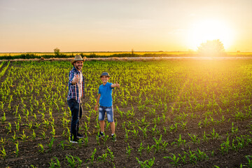 Family farmers are standing in their growing corn field. They are satisfied with progress of plants.
