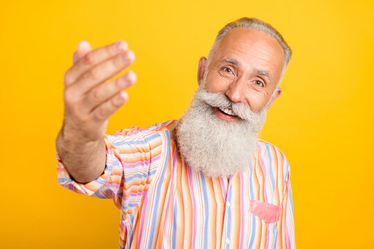 Photo of hospitable retired man show invite gesture wear striped shirt isolated yellow color background