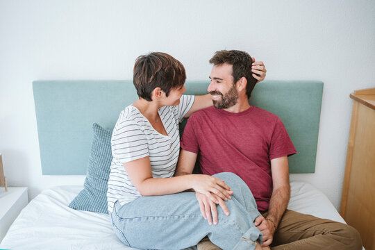 Woman looking at man while sitting together on bed at home