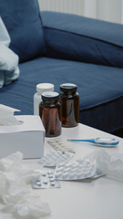 Close up of empty living room with medical treatment on table. Nobody in space with medicaments, medicine, bottles of pills, capsules, thermometer and tissues for patient with disease