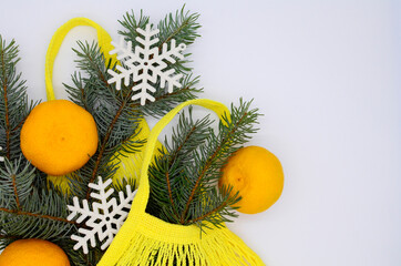 Three clementines in yellow eco string shopping bag with Christmas tree branch and snowflakes on...