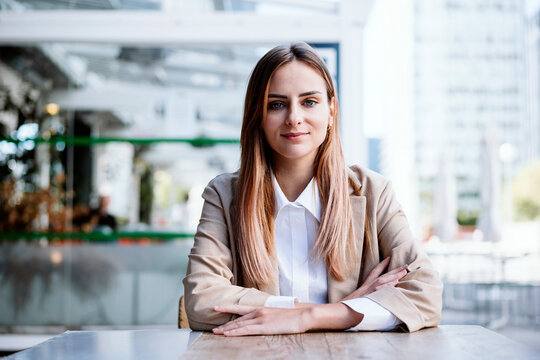 Smiling businesswoman with arms crossed sitting at cafe table