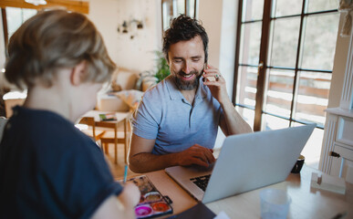 Mid adult father with small son working indoors at home, painting pictures and home office concept.