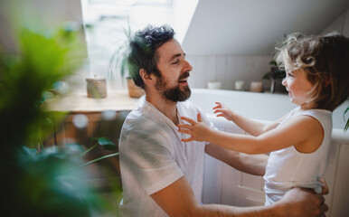 Mature father with small daughter indoors at home, getting ready for a bath.