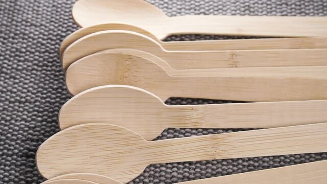 Eco-friendly wooden spoons made of bamboo falling on a gray rustic rough jute burlap. Ecological disposable utensils. Slow motion